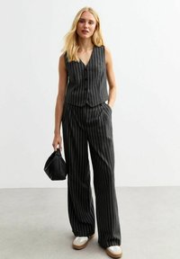 Grijs gestreept vest en brede broekset gemaakt van textuurstof. De outfit heeft een v-hals en knoopsluiting, gecombineerd met een zwarte handtas.