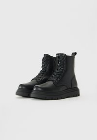 Un par de botas de cuero negro de cordones hasta el tobillo con cremallera lateral y suelas de goma gruesas sobre un fondo claro y liso.