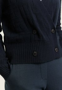 Navy knitted cardigan featuring a textured pattern, double-breasted design with four black buttons, and ribbed hem and cuffs.