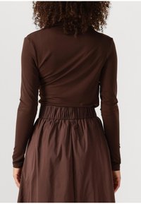 Bruine langmouwen top met een getailleerd ontwerp, gecombineerd met een vloeiende bruine rok met een elastische tailleband en een geplooide textuur aan de achterkant.