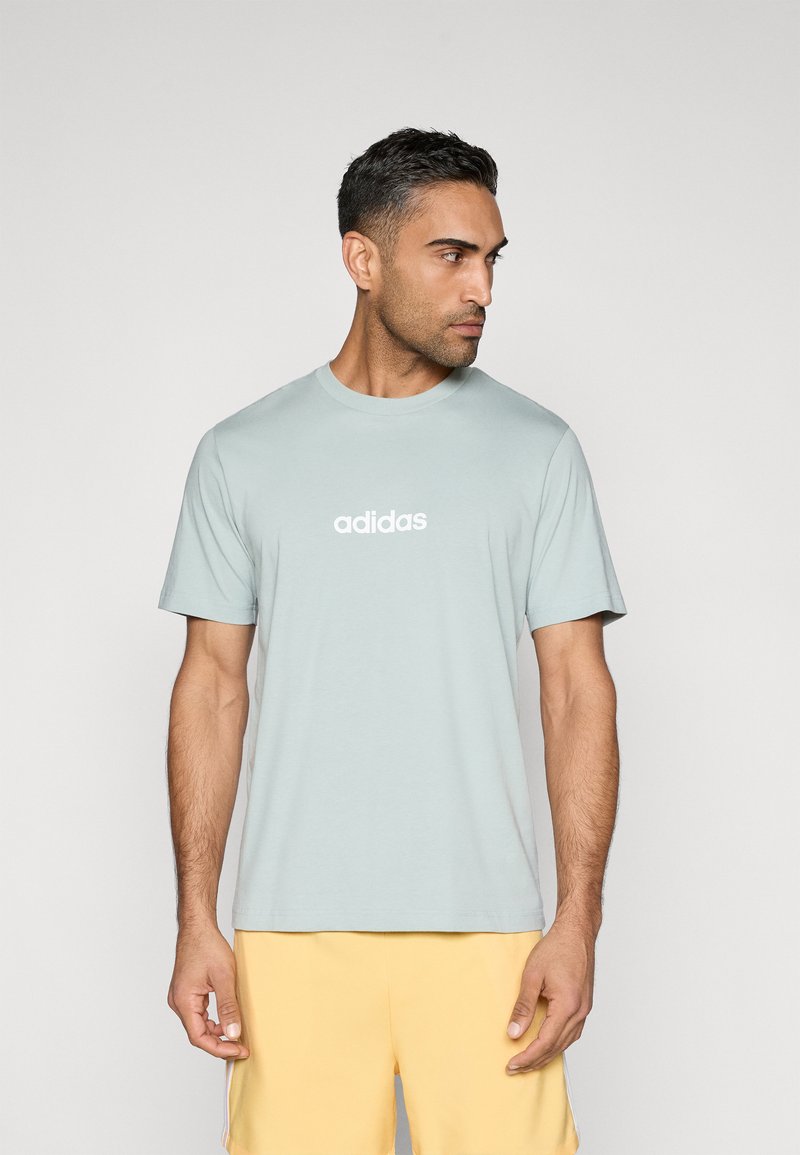 Helesinine puuvillane T-särk, millel on lühikesed varrukad ja ümar kaelus, ning valge "adidas" logo rinnal.