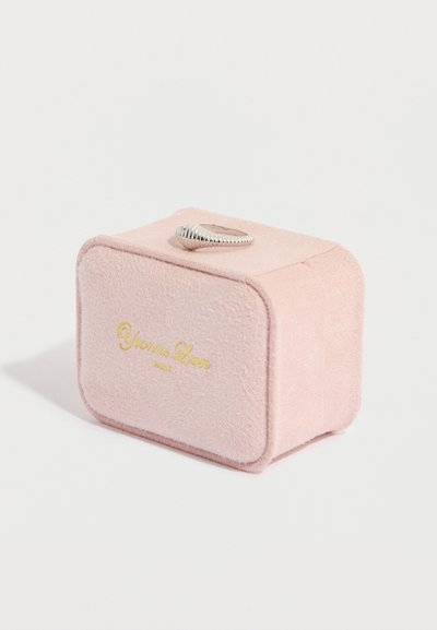 Scatola per gioielli in suede rosa con bordi arrotondati, logo dorato sulla parte anteriore e anello d'argento sul coperchio. Texture morbida e forma compatta.