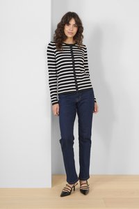 Cardigan rayé noir et blanc avec fermeture à boutons, associé à un jean bleu foncé et des chaussures à talons noires. Texture lisse, design ajusté.