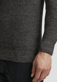 Gray knitted sweater with a textured pattern, featuring a crew neck and fitted cuffs, displayed on a person’s arm against a neutral background.