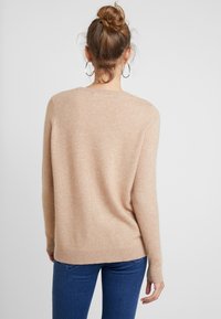 Beige gestrickter Pullover mit langen Ärmeln und rundem Ausschnitt, mit einem lockeren Schnitt und geripptem Saum, kombiniert mit blauen Jeans.