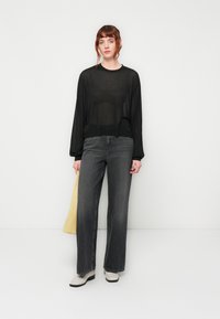 Haut transparent à manches longues noir, coupe ample, associé à un jean large taille haute gris foncé et des bottines blanches cassées. Sac fourre-tout jaune inclus.