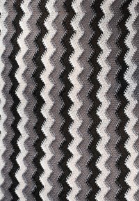Motif de tissu en maille zigzag avec des rayures ondulées alternées en noir, blanc, gris et beige.