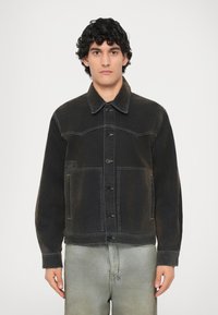 Giacca in denim nero con chiusura a bottoni, colletto a punta e due tasche sul petto. Presenta cuciture a contrasto e una texture leggermente sbiadita.