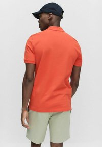 Kortærmet polo T-shirt i lys orange, lavet af glat bomuld. Sammen med lysegrønne shorts, der viser en afslappet pasform og et baggyldigt syn.