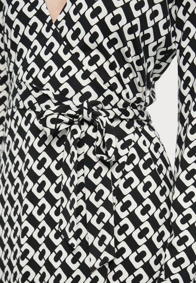 Φόρεμα τύπου wrap με ασπρόμαυρο γεωμετρικό σχέδιο, μακριά μανίκια, ζωνάκι στη μέση και βαθύ V στο ντεκολτέ. Λείο ύφασμα, casual σχεδιασμός.