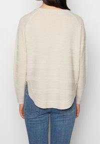 Maglione beige a maglia con un motivo a righe testurizzato, vestibilità rilassata e orlo inferiore arrotondato, abbinato a jeans blu.