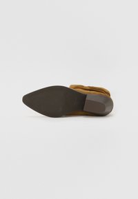 Brune suède ankelstøvle med spids tå og en glat gummisål. Har et samlet design ved anklen og en lav hæl.