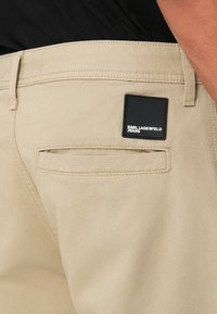 Bežinės medvilninės kelnės su užpakaline kišene ir juodu logotipu "KARL LAGERFELD JEANS". Lygi tekstūra su matomomis siūlėmis.