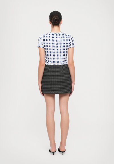 Tie-dye t-shirt in white and navy, paired with a fitted black mini skirt featuring a subtle houndstooth pattern. Low-heeled black shoes.