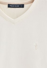 T-shirt di cotone color crema con scollo a V e logo ricamato sul petto. Tessuto morbido e design semplice, adatto per un abbigliamento casual.