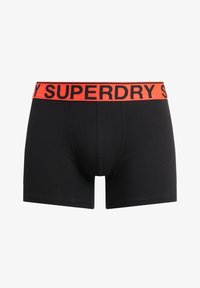Schwarze Boxershorts mit enger Passform, versehen mit einem orangenen elastischen Bund, der den Markennamen "SUPERDRY" in schwarzer Schrift zeigt.