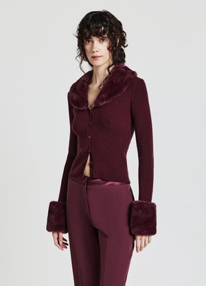 Cardigan ribbed bordeaux con colletto e polsini in pelliccia sintetica, caratterizzato da un design aderente e chiusura frontale con bottoni. Texture liscia e morbida.