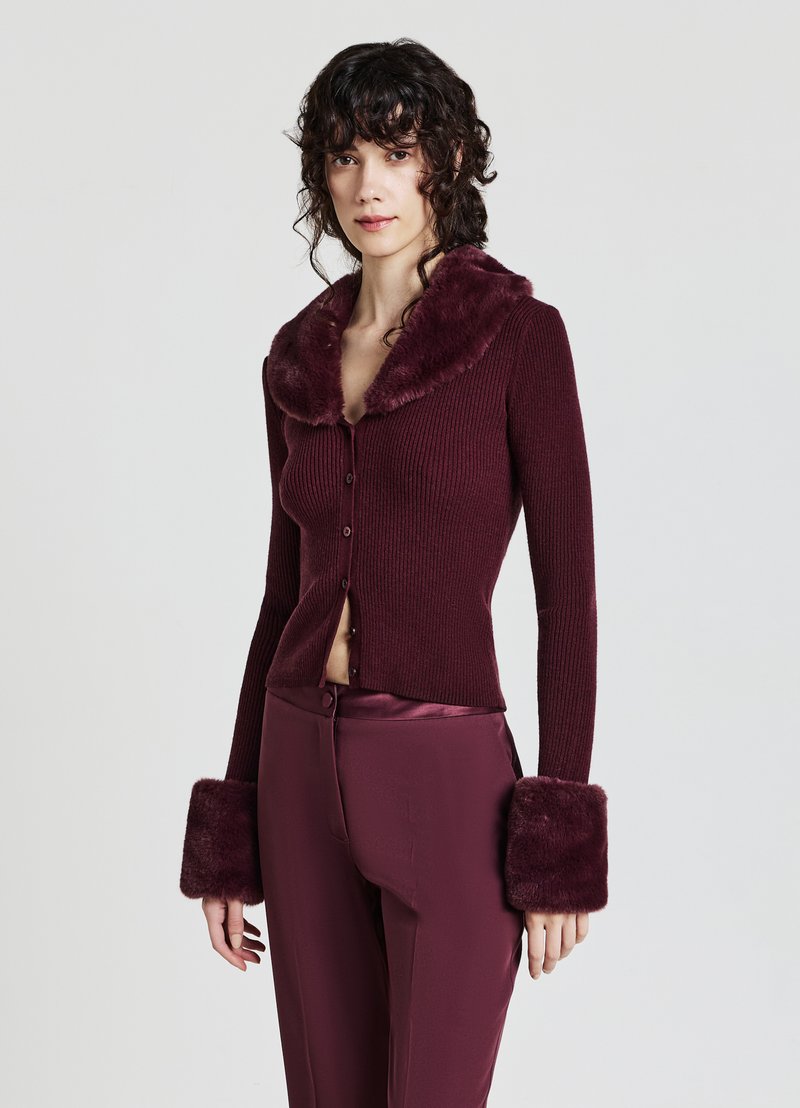 Burgunderfarbener, gerippter Cardigan mit einem Kragen und Manschetten aus Kunstfell, der über ein tailliertes Design und eine Knopfleiste verfügt. Glatte, weiche Textur.