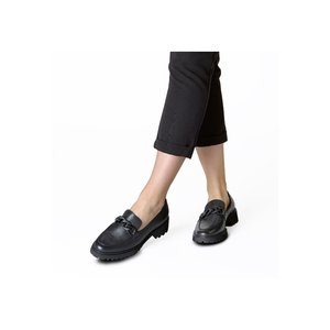 Beine in schwarzen, gekürzten Hosen und schwarzen, klobigen Loafers mit Kettendetail auf weißem Hintergrund.