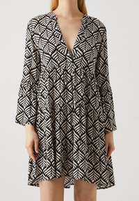 Vestido en blanco y negro con un patrón de hojas, con un profundo escote en V, dobladillo de volantes en capas y mangas acampanadas, hecho de tela ligera.