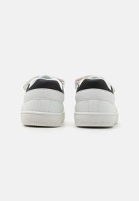 Baskets blanches avec des accents noirs, en matériau lisse. Présentent un design bas, une languette en textile et un logo en relief sur le talon.