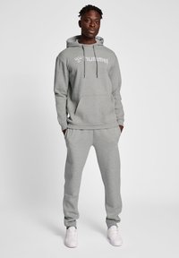 Grå bomullsblandning träningsdräkt med huvtröja, framficka och matchande joggers. Har en logotryck på bröstet och elastiska muddar.