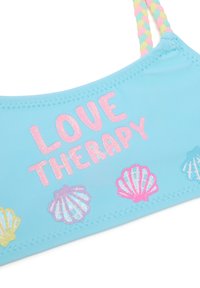 Top de baño azul claro con "LOVE THERAPY" en purpurina rosa. Presenta coloridos diseños de conchas en púrpura, rosa y amarillo. Tirantes trenzados.