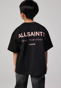 Juoda medvilninė marškinėliai su laisvu siluetu, turintys išskirtinį rožinį tekstą "ALLSAINTS" ir "LONDON" ant nugaros, su grafika.