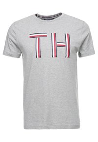 T-shirt gris à manches courtes avec de grandes lettres "TH" et des accents rayés bleu marine, rouge et blanc. Fabriqué en mélange de coton doux.
