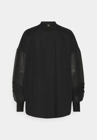 Chemise noire avec un corps en tissu solide et élégant. Manches bouffantes transparentes avec des accents superposés. L'encolure arrière est ornée d'un détail en forme de cœur doré.