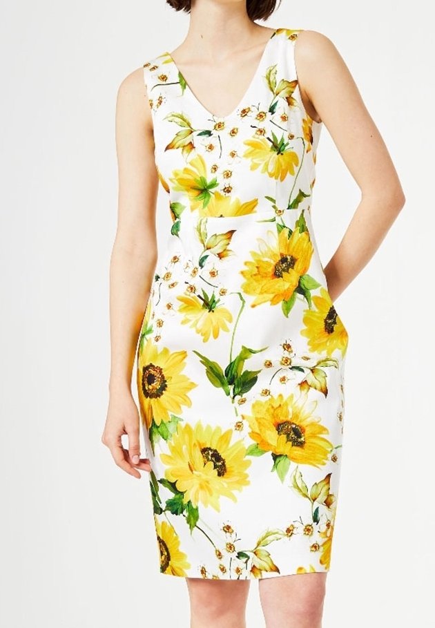 Robe blanche sans manches avec imprimé tournesol jaune vif et feuilles vertes, taille cintrée, portée par une personne avec une main dans la poche.