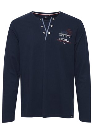 Námořnická košile s dlouhým rukávem a knoflíkovým výstřihem, s grafickým designem v bílé a červené barvě. Měkká tkanina, rovný střih, boční rozparky na spodním okraji.