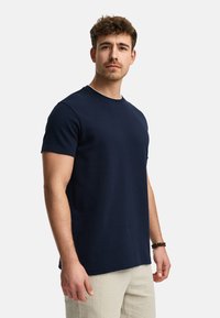 Camiseta de cuello redondo de color azul marino, hecha de un material de algodón suave, con mangas cortas y un ajuste relajado, con un patrón liso y sin logotipos visibles.