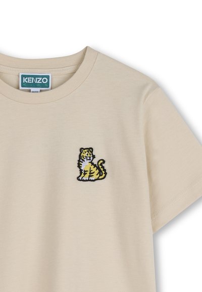 T-shirt in cotone beige con tigre gialla e bianca ricamata con bordo nero sul petto sinistro. Girocollo e maniche corte.