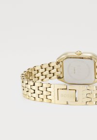 Montre-bracelet en métal doré avec un cadran carré, un bracelet en maillons et un fermoir avec le logo "BOSS". Fini lisse et design minimaliste.