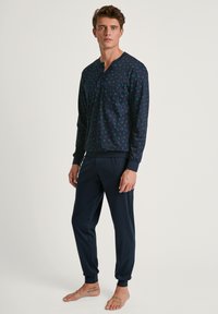 Marineblaues Schlafanzugset mit langärmligem Oberteil, das eine Brusttasche und ein grafisches Muster aufweist, kombiniert mit schmalen Hosen mit gerippten Bündchen.