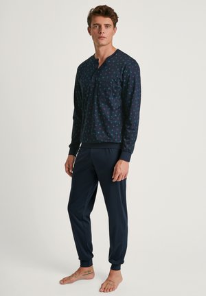 Ensemble de pyjama marine comprenant un haut à manches longues avec une poche sur la poitrine et un motif graphique, associé à un pantalon ajusté avec des poignets côtelés.