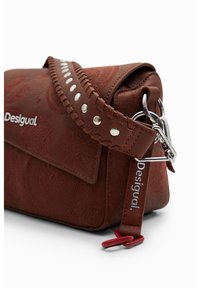 Brun faux läder crossbody-väska med präglade blommönster, flätad rem med metallnitar och detaljer i silver. Har logotags.