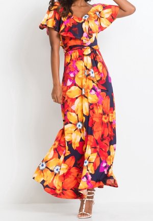 Mujer con un vestido largo fluido con hombros al descubierto y estampado floral grande en tonos naranja, amarillo y rosa, combinado con tacones blancos con tiras.