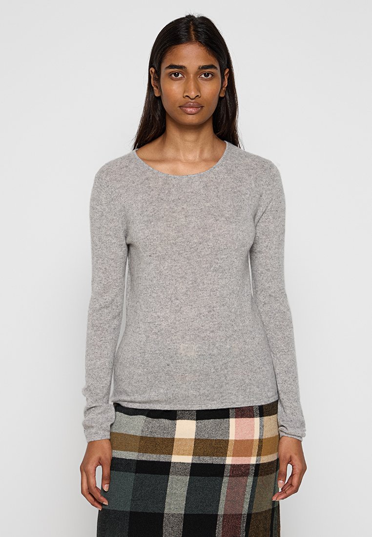 Maglione lungo grigio chiaro a manica lunga in materiale morbido con scollatura rotonda. Abbinato a una gonna a quadri con tonalità marroni, beige e nere.