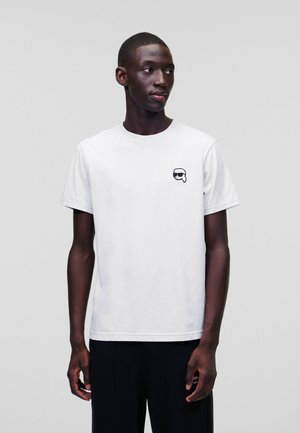 Witte katoenen T-shirt met een ronde hals en korte mouwen. Bevat een zwart grafisch logo op de linkerborst. Eenvoudig, minimalistisch design.
