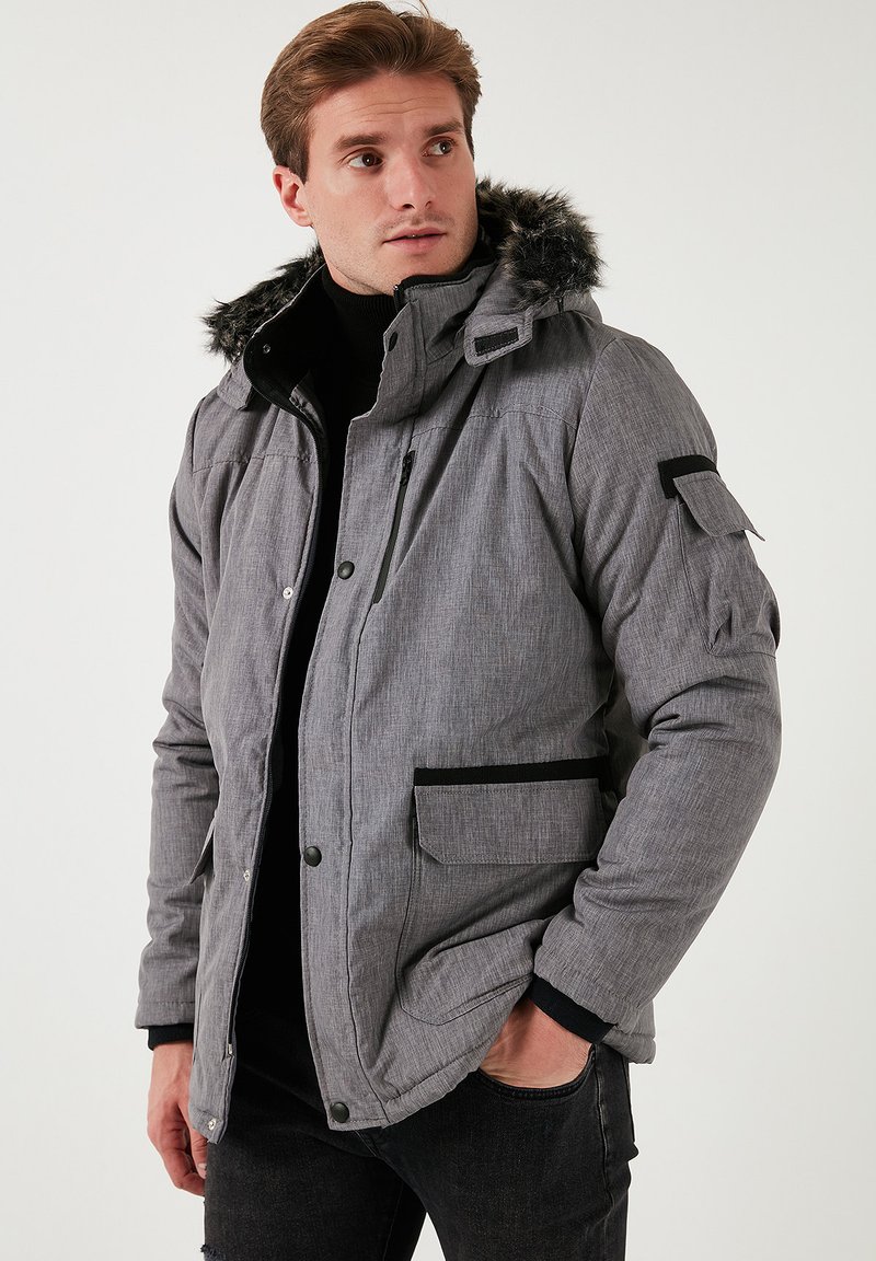 Jachetă puffer gri, cu țesătură texturată, margini negre, glugă căptușită cu blănă și multiple buzunare. Dispune de un buzunar pe piept cu fermoar și capse.