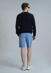 Marine gebreide trui, lichtblauwe shorts en witte sneakers. De shorts hebben een gladde textuur en achterzakken, terwijl de sneakers een modern ontwerp hebben.