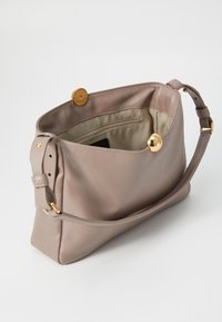 Light beige leather handbag with a golden snap closure, a single adjustable strap, and a textured interior pocket. Smooth, structured design.
