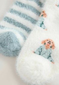 Two pairs of fluffy socks: one features blue and white stripes, the other is white with a colorful animal pattern and round pom-pom accents.