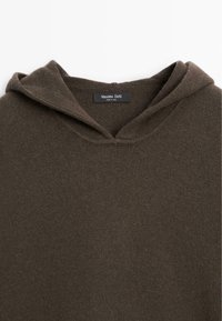 Bruine hoodie van zacht materiaal met een gestructureerde afwerking. Heeft een v-hals en een merklabel in het nekgebied.