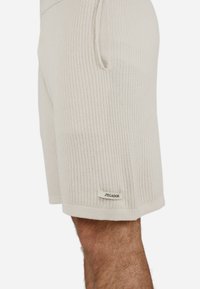 Ribbed beige shorts made of soft fabric, featuring side pockets and a small tag with "PEGADOR" at the hem.