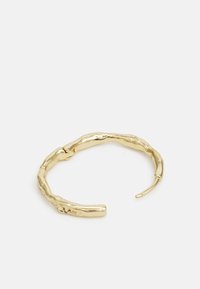 Bracelet jonc en métal doré avec un design organique texturé ressemblant à des branches torsadées. Ouvert aux deux extrémités pour un ajustement modifiable.