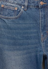 Jeans de mezclilla azul oscuro con un diseño clásico de cinco bolsillos, remaches de cobre, costuras en contraste y una textura ligeramente deslavada.