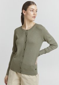 Olivově zelený kardigan s kulatým výstřihem, zapínáním na knoflíky, dlouhými rukávy a žebrovaným lemem. Měkká pletená textura s malým logem.